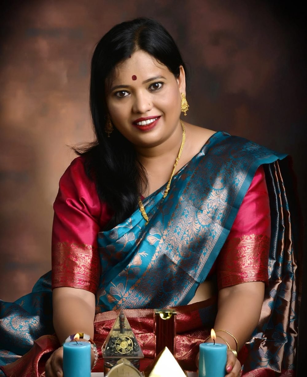 Dr. Abha Jain in a teal and red silk saree, seated with candles and Vastu pyramids
